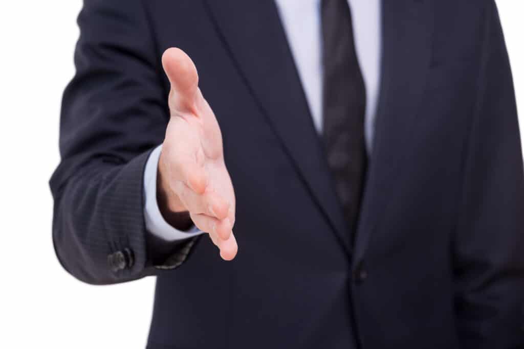 Welcome on board! Close-up of businessmen stretching out hand for shaking while standing against grey background