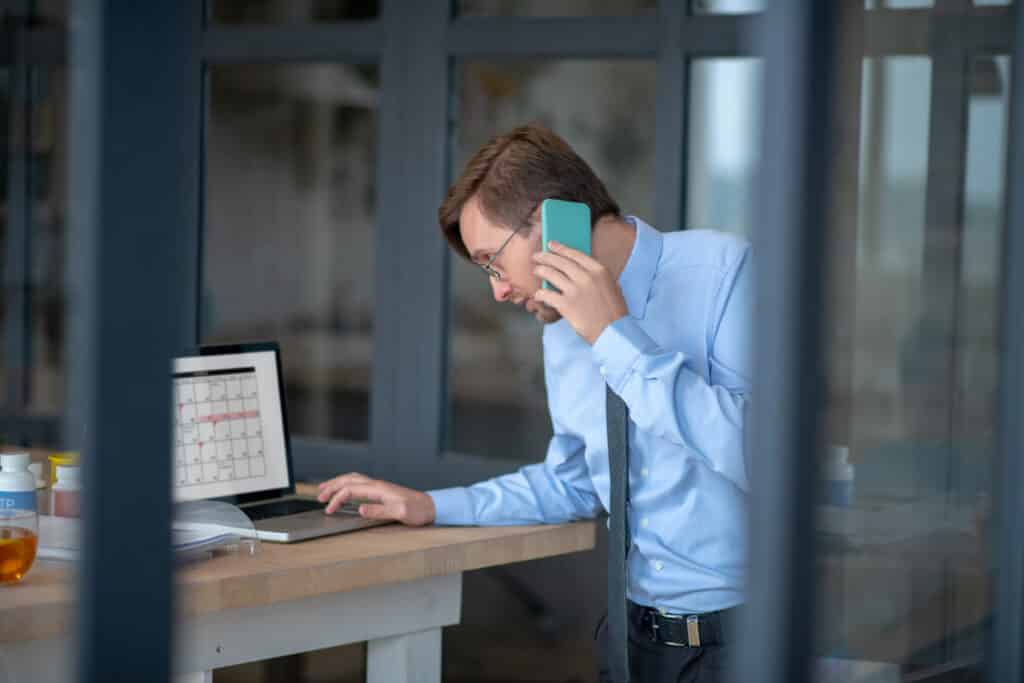 Schedule on laptop. Busy businessman checking his schedule on laptop while calling secretary