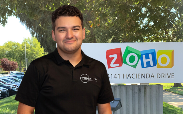 George Hamelin, a developer at Zenatta Consulting in front of a sign with the Zoho logo on it